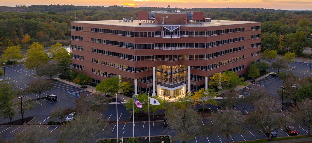 Aerial view of an office building bathed in warm hues during sunset, showcasing its architectural design and surroundings.